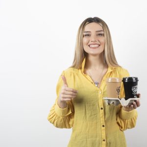 Portrait of young woman holding cups of coffee and giving thumbs up. High quality photo